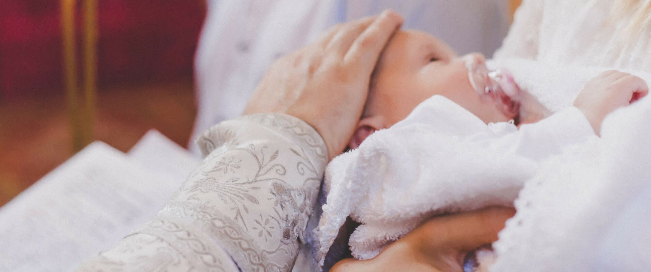 Pfarrer hält Hand auf Kopf vom Kind bei Taufe